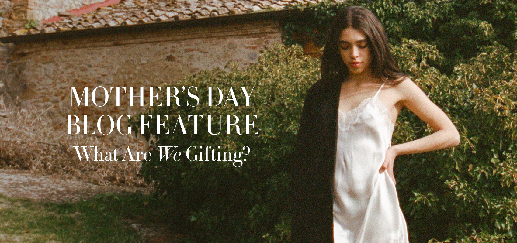 Image of brunette woman wearing the Journelle Celine Silk Slip in white with a blazer draped over one shoulder. She is outside against a stone building and plants. Text says: Mother's Day Blog Feature: What Are We Gifting?